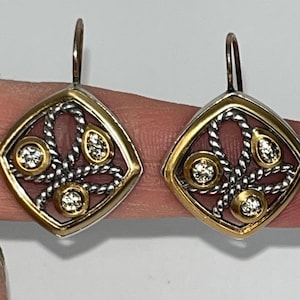 K&ouml;nnte beinhalten: Ein Paar Ohrringe mit Diamantakzenten. Jeder Ohrring hat einen goldfarbenen quadratischen Rahmen mit einem silberfarbenen Seildesign und drei diamantartigen Akzenten. Die Ohrringe werden von einem Finger gehalten.