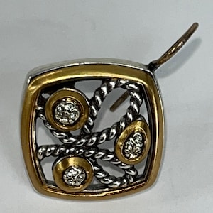 K&ouml;nnte beinhalten: Ein quadratischer Ohrring mit silbernem und goldenem Design. Der Ohrring hat einen goldenen Rand, ein silbernes seilartiges Muster und drei goldgerahmte Kreise mit kleinen, klaren Steinen. Der Ohrringstift ist sichtbar.