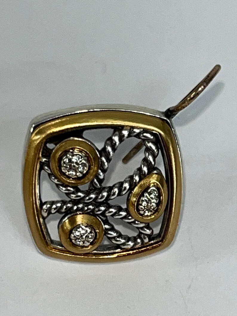 K&ouml;nnte beinhalten: Ein quadratischer Ohrring mit silbernem und goldenem Design. Der Ohrring hat einen goldenen Rand, ein silbernes seilartiges Muster und drei goldgerahmte Kreise mit kleinen, klaren Steinen. Der Ohrringstift ist sichtbar.