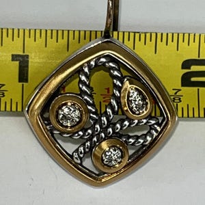 K&ouml;nnte beinhalten: Ein gold-silberner Anh&auml;nger mit einem diamantartigen Edelstein-Design. Der Anh&auml;nger ist quadratisch mit einem goldenen Rand und einem silbernen seilartigen Design in der Mitte. Drei goldene Kreise mit Edelsteinen sind in das Design eingesetzt. Der Anh&auml;nger ist etwa 2,5 cm lang.