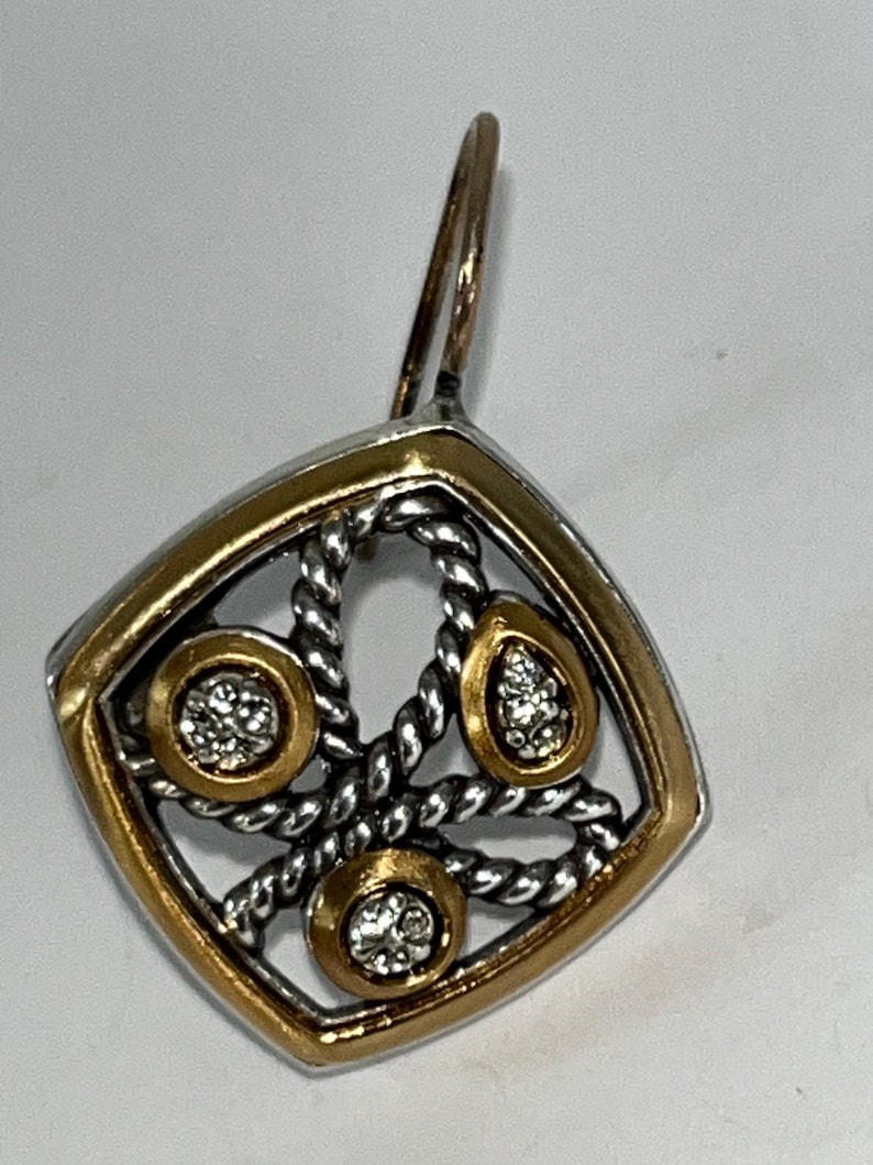 K&ouml;nnte beinhalten: Einzelner Ohrring mit Gold- und Silberdesign. Der Ohrring hat einen quadratischen Rahmen mit goldenem Rand, der ein silbernes, seilartiges Muster umschlie&szlig;t. Drei goldgerahmte Fassungen halten klare Edelsteine.