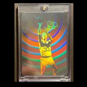 Peut inclure: Une carte de collection de basket-ball dans un étui en plastique transparent. La carte présente un joueur en uniforme jaune avec le numéro 33, sur un fond holographique coloré. La carte est dans un étui de protection.