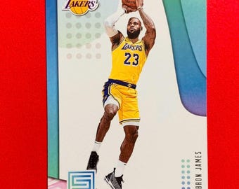 Op de afbeelding: Een basketbal trading card met LeBron James in een geel en paars Los Angeles Lakers uniform. De kaart heeft een blauw-witte achtergrond met het Lakers logo en de naam van de speler.