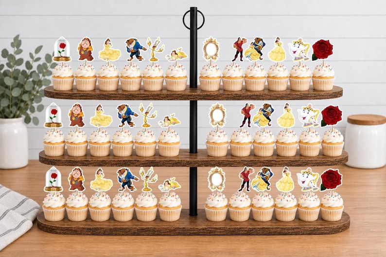 May include: A three-tiered wooden cupcake stand holding rows of cupcakes topped with paper cutouts featuring characters and objects from Beauty and the Beast, including a red rose, a mirror, a teapot, and figures of Belle and the Beast.