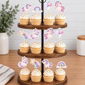 May include: A three-tiered wooden cupcake stand holding twelve cupcakes topped with white frosting and colourful sprinkles. Each cupcake features a decorative paper topper depicting unicorns, rainbows, shooting stars, or clusters of balloons.