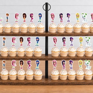 May include: A three-tiered wooden cupcake stand holding numerous cupcakes topped with Strawberry Shortcake character paper toppers. Each cupcake features a decorative cutout of a character or a sign with the text Strawberry Shortcake.