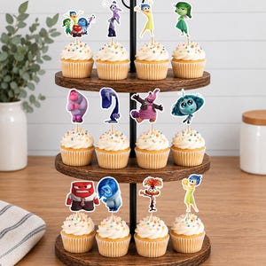 May include: A three-tiered wooden stand holding twelve cupcakes topped with colorful sprinkles and paper character toppers from the movie Inside Out. The toppers feature various animated figures including Joy, Sadness, Anger, Disgust, Fear, and Anxiety.