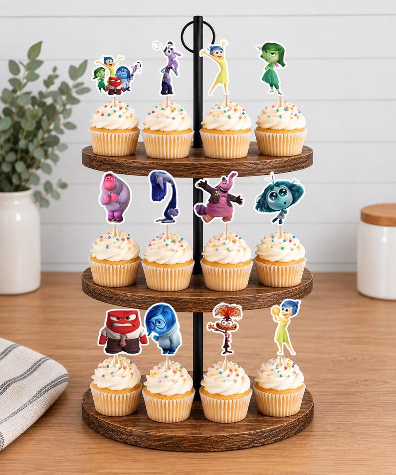 May include: A three-tiered wooden stand holding twelve cupcakes topped with colorful sprinkles and paper character toppers from the movie Inside Out. The toppers feature various animated figures including Joy, Sadness, Anger, Disgust, Fear, and Anxiety.