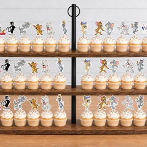 Peut inclure: Un pr&eacute;sentoir &agrave; cupcakes en bois &agrave; trois niveaux contenant de nombreux cupcakes surmont&eacute;s de d&eacute;coupes en papier repr&eacute;sentant les personnages de Tom et Jerry. Chaque cupcake poss&egrave;de une d&eacute;coration illustrant divers personnages du dessin anim&eacute;.