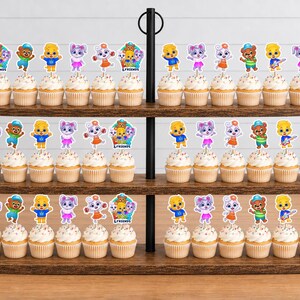 May include: A three-tiered wooden cupcake stand holding numerous cupcakes topped with colourful cartoon character paper toppers. The toppers feature various animal and human figures, including some labelled with the text "Lulu & Friends".