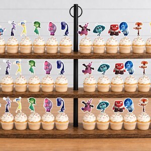 May include: A three-tiered wooden cupcake stand holding thirty-six cupcakes, each topped with a small paper cutout of characters from the movie Inside Out. The characters include Joy, Sadness, Anger, Disgust, Fear, Bing Bong, and others.