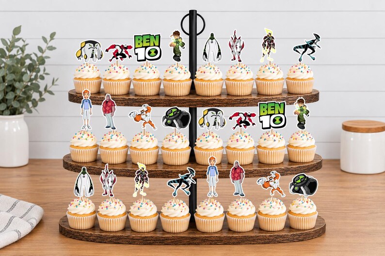 May include: A three-tiered wooden cupcake stand holding twenty-four cupcakes topped with Ben 10 character paper toppers. The toppers feature various alien figures, the Ben 10 logo, and human characters, all printed in full colour on white cardstock.