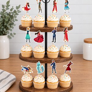 Op de afbeelding: Een houten cupcake-standaard met drie niveaus en twaalf cupcakes, elk voorzien van een decoratieve papieren uitsparing met diverse geanimeerde figuren in kleurrijke outfits, waaronder een gevleugeld wezen, een blauwe vos en verschillende mensen.