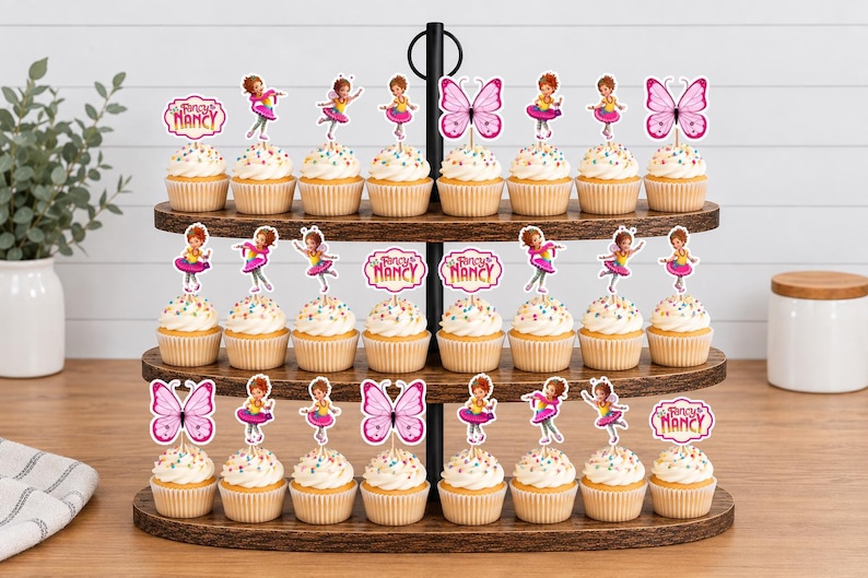 May include: A three-tiered wooden stand holding twenty-four cupcakes topped with Fancy Nancy themed paper decorations. The toppers feature illustrations of a girl in a pink outfit, pink butterflies, and the Fancy Nancy logo in pink and white.