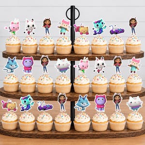 May include: A three-tiered wooden cupcake stand holding twenty-four cupcakes, each topped with a colorful paper cutout featuring characters from Gabby's Dollhouse, including Gabby, Pandy Paws, Cakey, MerCat, DJ Catnip, and other feline friends.