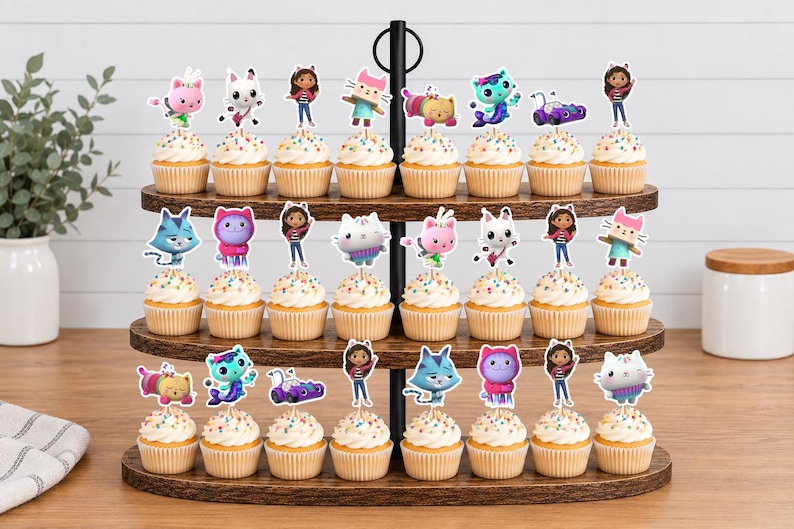 May include: A three-tiered wooden cupcake stand holding twenty-four cupcakes, each topped with a colorful paper cutout featuring characters from Gabby's Dollhouse, including Gabby, Pandy Paws, Cakey, MerCat, DJ Catnip, and other feline friends.