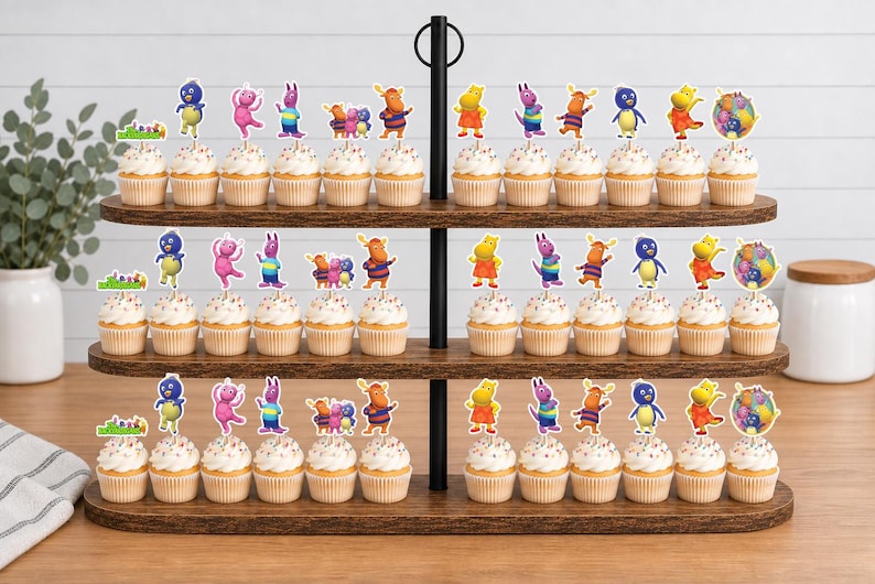 May include: A three-tiered wooden cupcake stand holding numerous cupcakes topped with colorful paper cutouts of cartoon characters from The Backyardigans, including Pablo, Tyrone, Uniqua, Tasha, and Austin, along with circular logo toppers.