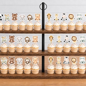 K&ouml;nnte beinhalten: Ein dreist&ouml;ckiger Cupcake-St&auml;nder aus Holz mit Reihen von Cupcakes, die mit Papieraufstellern von Safaritieren wie Pandas, B&auml;ren, Affen, Tigern, Giraffen, Zebras, L&ouml;wen und Entdeckern verziert sind, die in einem sich wiederholenden Muster angeordnet sind.