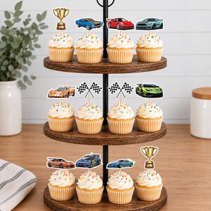 May include: A three-tiered wooden cupcake stand holding twelve cupcakes topped with colorful sprinkles. The cupcakes are decorated with paper toppers featuring various sports cars, checkered racing flags, and gold-colored trophy cups.