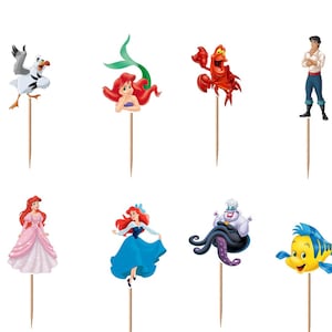 Puede incluir: Un conjunto de doce adornos para cupcakes con varios personajes de La Sirenita, incluyendo a Ariel en diferentes poses, Sebasti&aacute;n, Flounder, el Rey Trit&oacute;n, &Uacute;rsula y el Pr&iacute;ncipe Eric, cada uno unido a un palillo de madera fino.