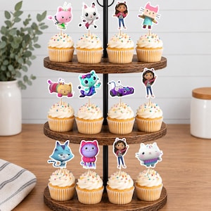May include: A three-tiered wooden cupcake stand holding twelve cupcakes, each topped with a decorative paper cutout featuring colorful cartoon characters, including cats, a girl with cat ears, and a purple vehicle, all with rainbow sprinkles.
