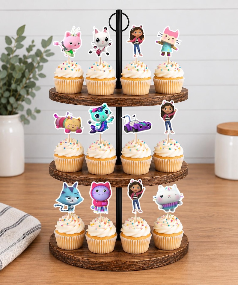 May include: A three-tiered wooden cupcake stand holding twelve cupcakes, each topped with a decorative paper cutout featuring colorful cartoon characters, including cats, a girl with cat ears, and a purple vehicle, all with rainbow sprinkles.