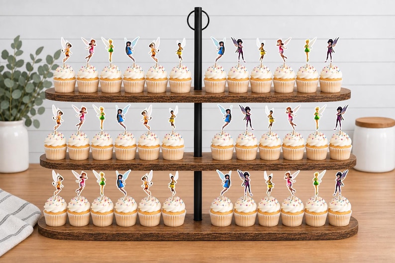 May include: A three-tiered wooden cupcake stand holding numerous cupcakes topped with colorful fairy-shaped paper decorations. The stand features a central black metal pole with a circular handle at the top, displaying rows of treats with various fairy figures.