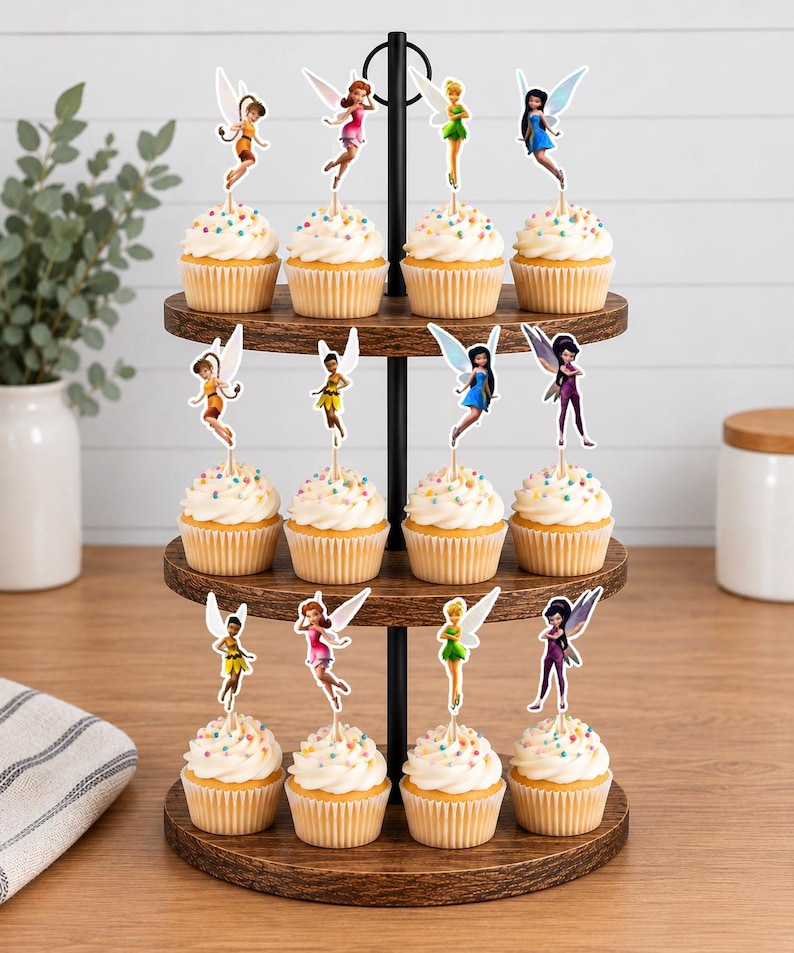 May include: A three-tiered wooden cupcake stand holding twelve cupcakes, each topped with a decorative fairy cutout. The cupcakes feature white frosting with colorful sprinkles. The stand has a black metal central pole and circular wooden shelves.