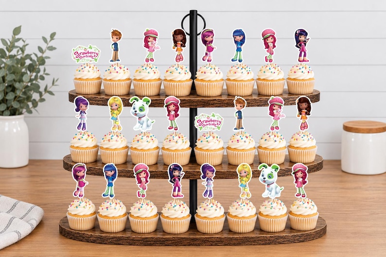 May include: A three-tiered wooden cupcake stand holding twenty-four cupcakes topped with colorful Strawberry Shortcake character paper toppers. Each cupcake features a unique character cutout or a Strawberry Shortcake logo sign.