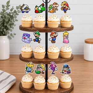 May include: A three-tiered wooden cupcake stand holding twelve cupcakes, each topped with a colorful paper cutout of a video game character. The characters include Mario, Luigi, Princess Peach, Bowser, Yoshi, and various other figures on wooden picks.