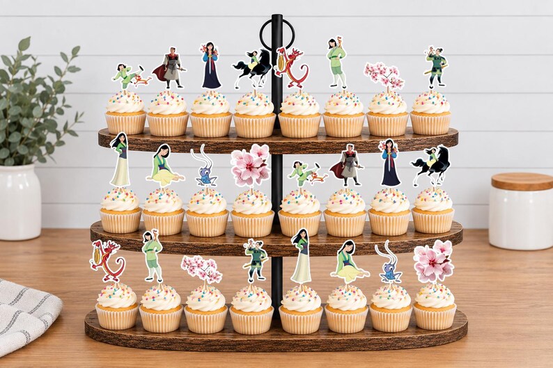 Peut inclure: Un pr&eacute;sentoir &agrave; cupcakes en bois &agrave; trois niveaux contenant vingt-quatre cupcakes, chacun surmont&eacute; d'une d&eacute;coupe en papier d&eacute;corative repr&eacute;sentant des personnages et des motifs de fleurs de cerisier du film Mulan, dont Mushu, Li Shang et Mulan.