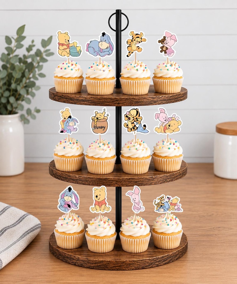 May include: A three-tiered wooden cupcake stand holding twelve cupcakes topped with white frosting and colorful sprinkles. Each cupcake features a paper topper depicting Winnie the Pooh characters including Pooh, Eeyore, Tigger, and Piglet in various poses.