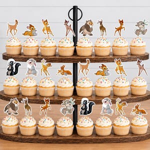 May include: A three-tiered wooden cupcake stand holding twenty-four cupcakes, each topped with a paper cutout of a forest animal character. The characters include deer, rabbits, and skunks, featuring various poses and colors like brown, tan, and white.