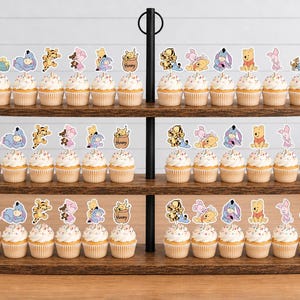 May include: A three-tiered wooden display stand holding numerous cupcakes topped with paper cutouts of Winnie the Pooh characters including Tigger, Piglet, and Eeyore. Each cupcake features a white frosting swirl and a decorative character topper.