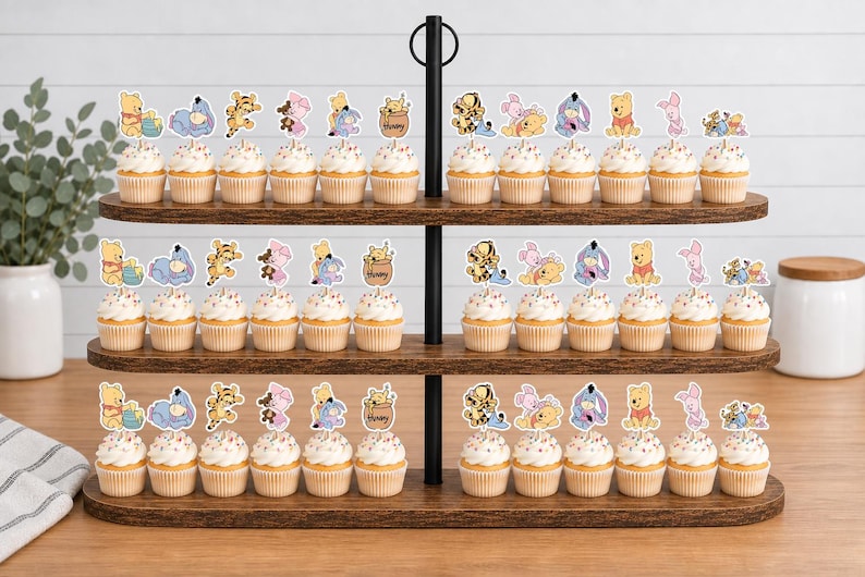May include: A three-tiered wooden display stand holding numerous cupcakes topped with paper cutouts of Winnie the Pooh characters including Tigger, Piglet, and Eeyore. Each cupcake features a white frosting swirl and a decorative character topper.