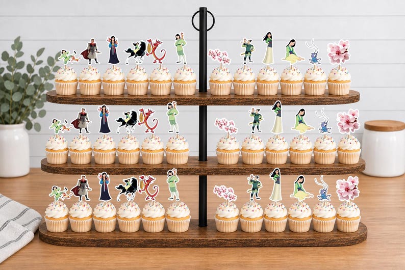 Peut inclure: Un pr&eacute;sentoir en bois &agrave; trois niveaux contenant des rang&eacute;es de cupcakes surmont&eacute;s de d&eacute;coupes en papier d&eacute;coratives repr&eacute;sentant des personnages et des motifs de fleurs de cerisier de l'histoire de Mulan, incluant un guerrier, un dragon et un cheval.