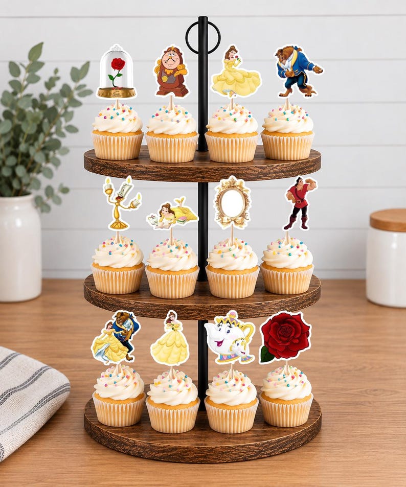 May include: A three-tiered wooden cupcake stand holding twelve cupcakes topped with white frosting and colorful sprinkles. Each cupcake features a decorative paper topper depicting characters and objects from Beauty and the Beast, including the rose, clock, and teapot.