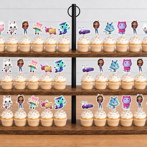 May include: A three-tiered wooden cupcake stand holding numerous cupcakes topped with colorful character toppers. The toppers feature various animated figures including a girl, cats, and other creatures in vibrant shades of pink, blue, and purple.