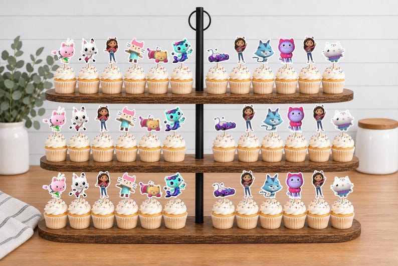 May include: A three-tiered wooden cupcake stand holding numerous cupcakes topped with colorful character toppers. The toppers feature various animated figures including a girl, cats, and other creatures in vibrant shades of pink, blue, and purple.