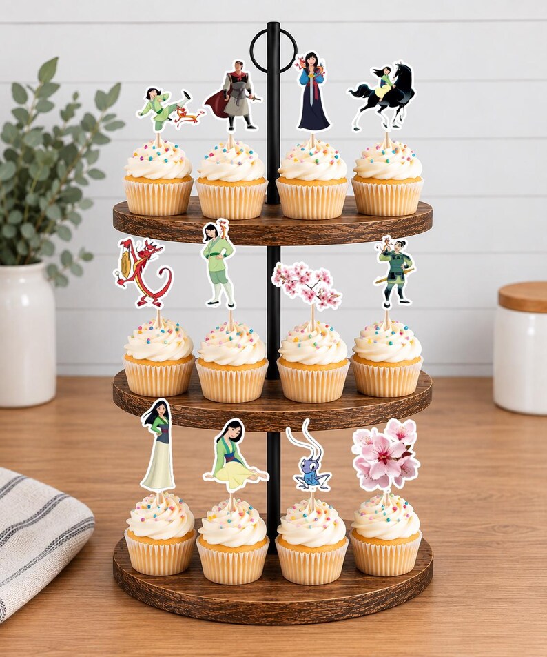 Peut inclure: Un pr&eacute;sentoir &agrave; cupcakes en bois &agrave; trois niveaux contenant douze cupcakes garnis de gla&ccedil;age blanc et de vermicelles color&eacute;s. Chaque cupcake est surmont&eacute; d'une d&eacute;coration en papier repr&eacute;sentant des personnages et des fleurs du film Mulan.