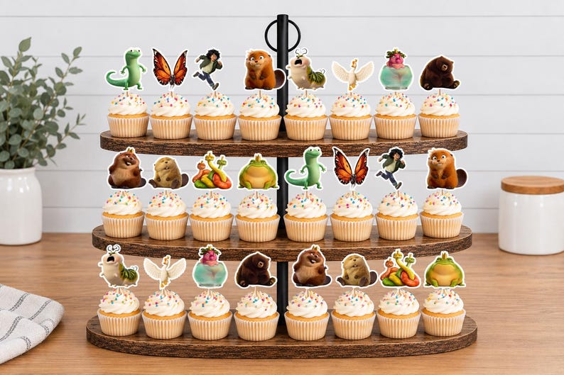 May include: A three-tiered wooden cupcake stand holding twenty-four cupcakes, each topped with a paper cutout featuring various animated characters, including a green lizard, a butterfly, a brown bear, a frog, and a white bird, with sprinkles.