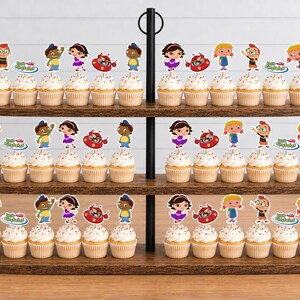 Puede incluir: Un soporte de madera para cupcakes de tres niveles con numerosos cupcakes decorados con figuras de papel de los Little Einsteins. Cada adorno muestra personajes de dibujos animados coloridos y el logotipo de Little Einsteins en los estantes.