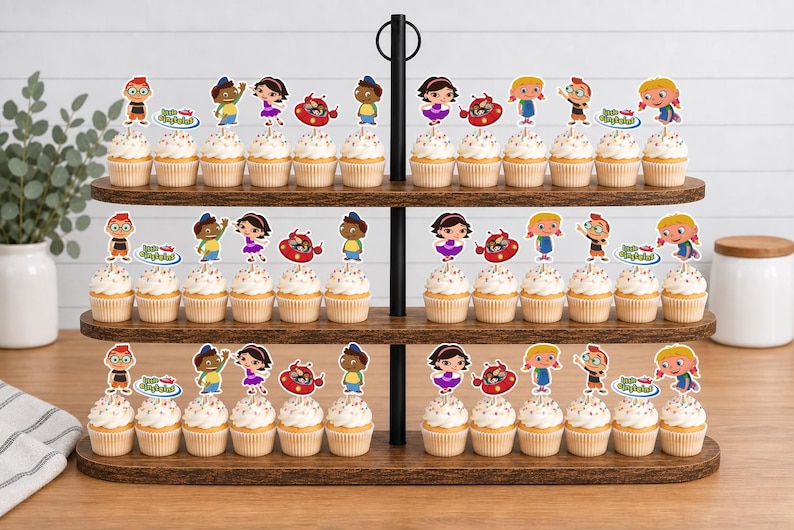 Puede incluir: Un soporte de madera para cupcakes de tres niveles con numerosos cupcakes decorados con figuras de papel de los Little Einsteins. Cada adorno muestra personajes de dibujos animados coloridos y el logotipo de Little Einsteins en los estantes.