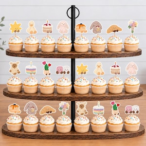Puede incluir: Un soporte de tres niveles de madera oscura con veinticuatro cupcakes. Cada cupcake tiene una cobertura de glaseado blanco, chispas de colores y un recorte de papel con ilustraciones de dibujos animados de animales y flores.