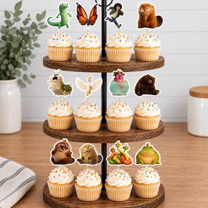 May include: A three-tiered wooden cupcake stand holding twelve cupcakes topped with white frosting and colorful sprinkles. Each cupcake features a decorative paper topper depicting various animated characters, including animals, a butterfly, and a person.