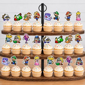 May include: A three-tiered wooden cupcake stand holding twenty-four cupcakes, each topped with a colorful paper cutout of various Super Mario characters including Mario, Luigi, Princess Peach, Yoshi, Bowser, and other iconic figures from the game series.