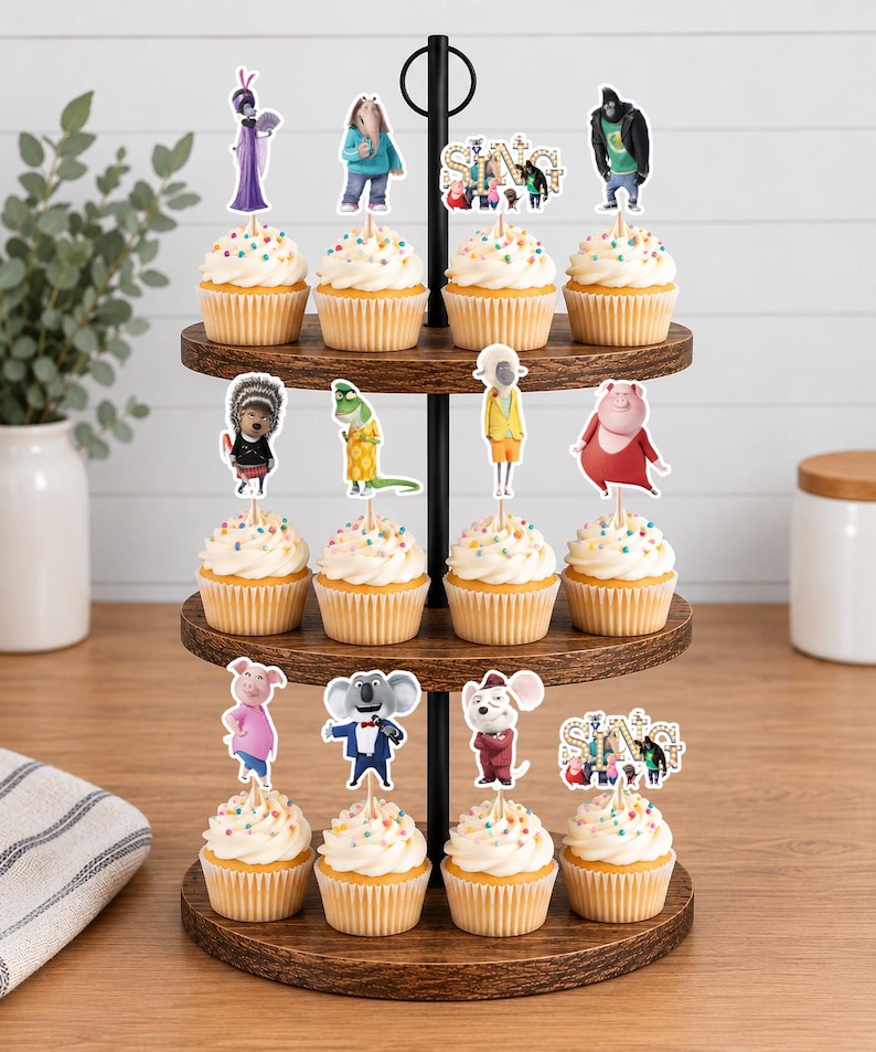 May include: A three-tiered wooden cupcake stand holding twelve cupcakes topped with white frosting and colorful sprinkles. Each cupcake features a paper topper depicting various animated characters from the movie Sing, including the Sing logo text.