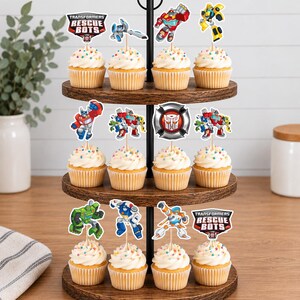 May include: A three-tiered wooden stand holding twelve cupcakes topped with white frosting and colorful sprinkles. Each cupcake features a paper topper depicting Transformers Rescue Bots characters, logos, and a silver Autobot emblem.