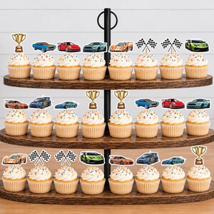 May include: A three-tiered wooden cupcake stand holding twenty-four cupcakes topped with paper cutouts featuring various colorful sports cars, gold trophies, and black and white checkered racing flags arranged in rows on each level.