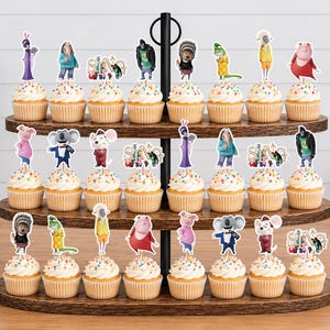 May include: A three-tiered wooden cupcake stand holding twenty-four cupcakes topped with white frosting and colorful sprinkles. Each cupcake features a paper topper depicting various animated characters from the movie Sing, including the Sing logo.